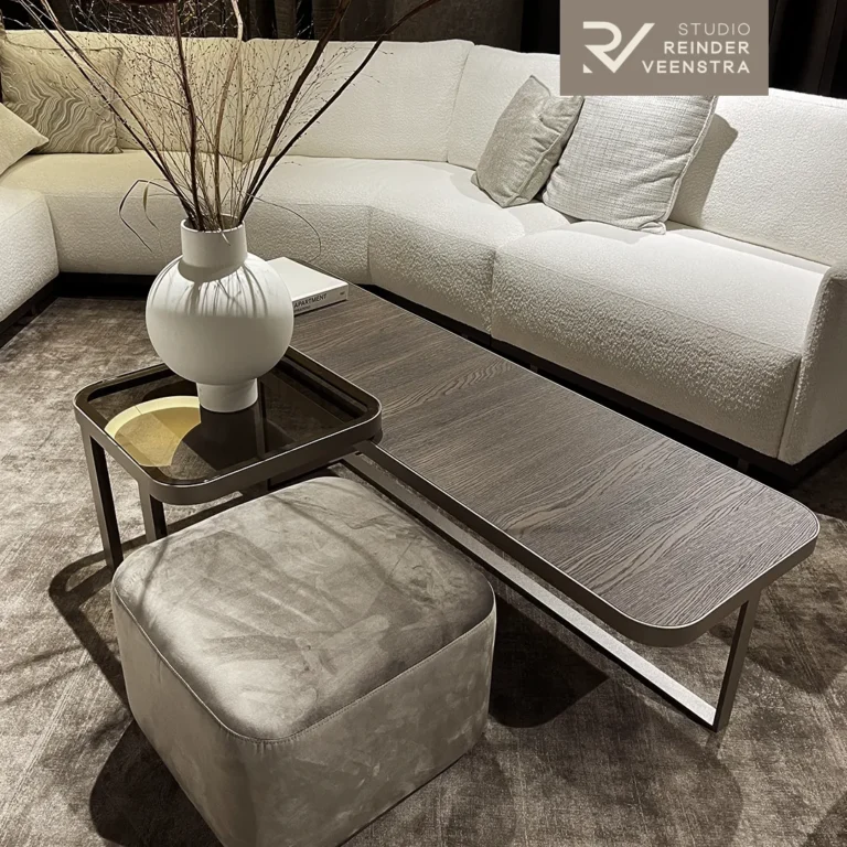 Seating area with a white bouclé corner sofa, a bronze-framed wooden coffee table, a velvet pouffe and a sculptural vase.